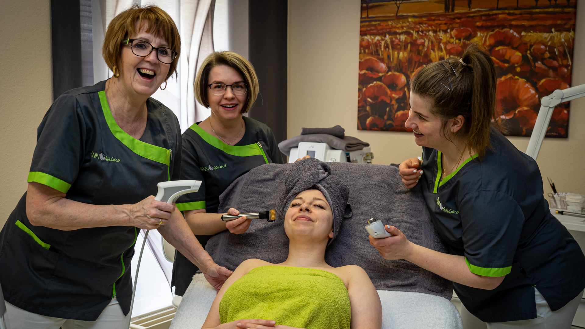 3 Kosmetikerinnen behandeln eine Kundin mit Geräten und lachen in die Kamera